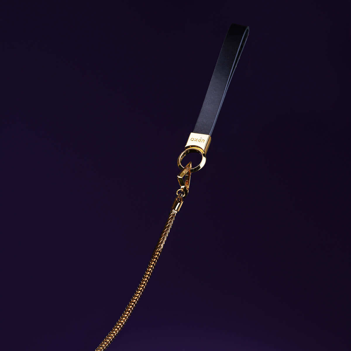 UPKO "Moist Eyes" Pearl Leash featuring a sleek black strap and elegant gold hardware against a dark background.