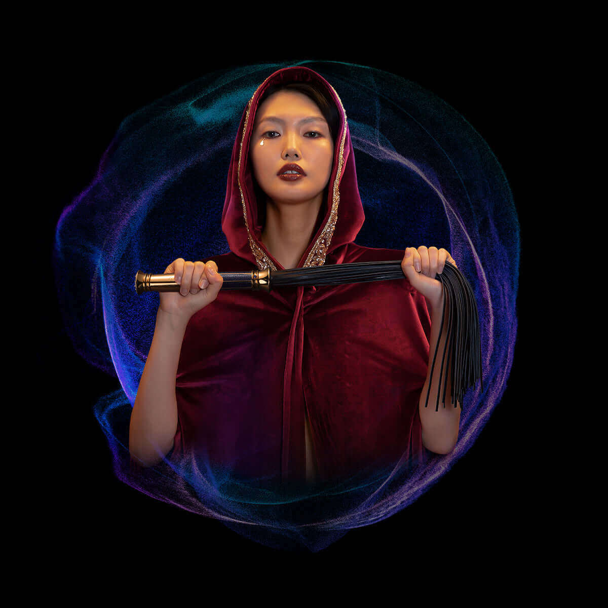 Woman in red cloak holding UPKO Black Label Collection flogger, set against a cosmic background, symbolizing intimacy and luxury.
