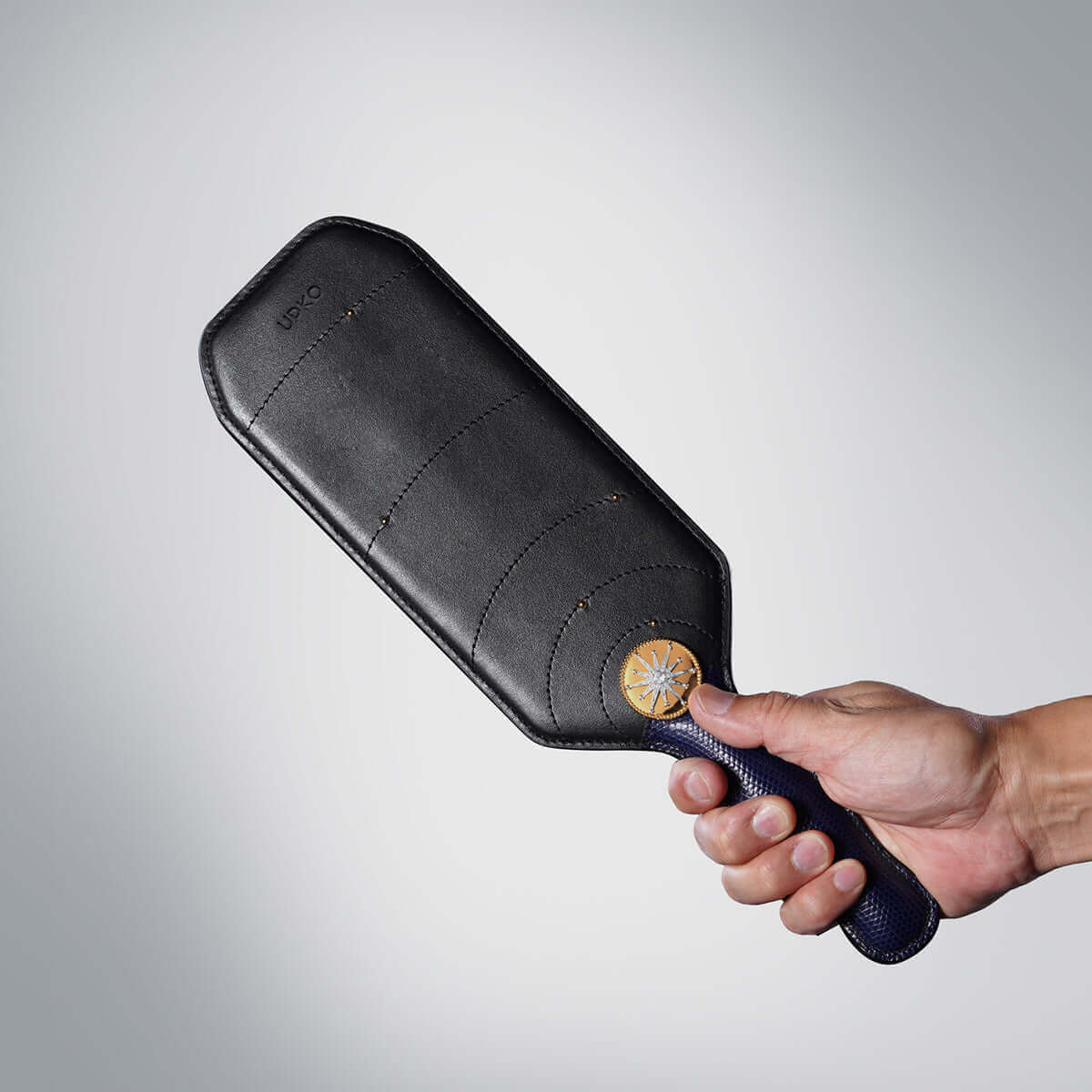 Hand holding UPKO Black Label Collection Paddle made from rare leather and luxury materials, showcasing exquisite craftsmanship.