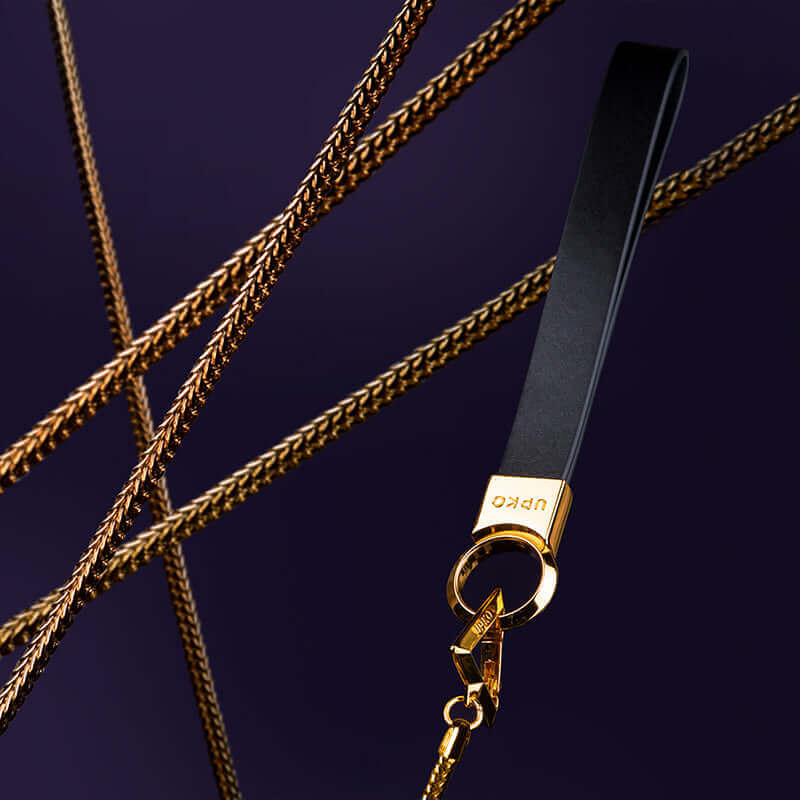 UPKO "Moist Eyes" Pearl Leash featuring a stylish black strap with gold accents and keyring against a dark background.