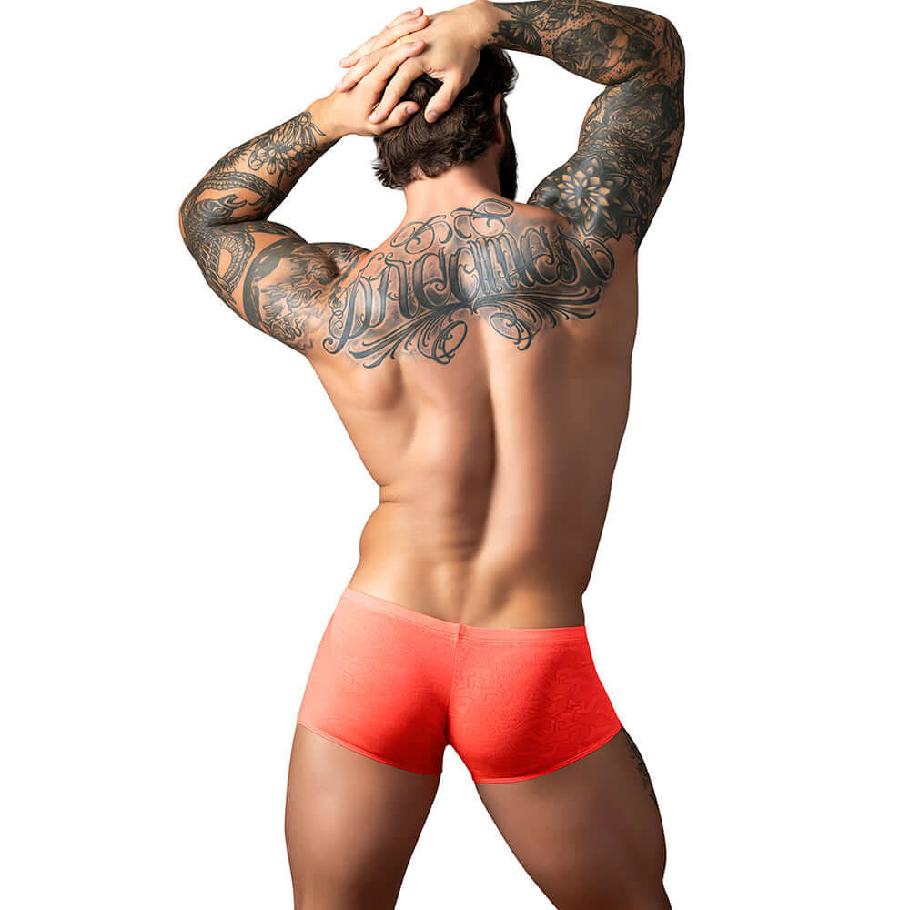 Model showcasing Male Power Kilauea Limited Edition Mini Short Coral L from the back, emphasizing bold style and tattoo details.