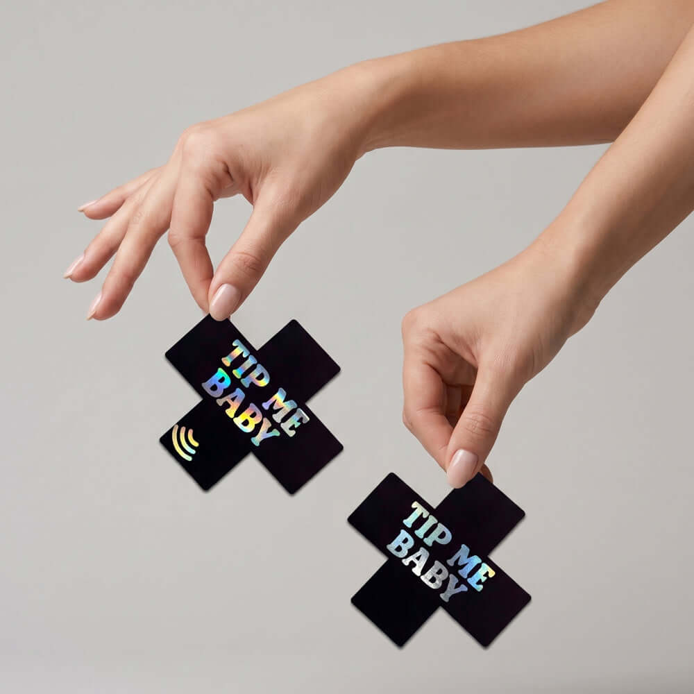 Two hands holding Neva Nude Tip Me Baby Holographic X Smart NFC Pasties, showcasing bold design and NFC technology.