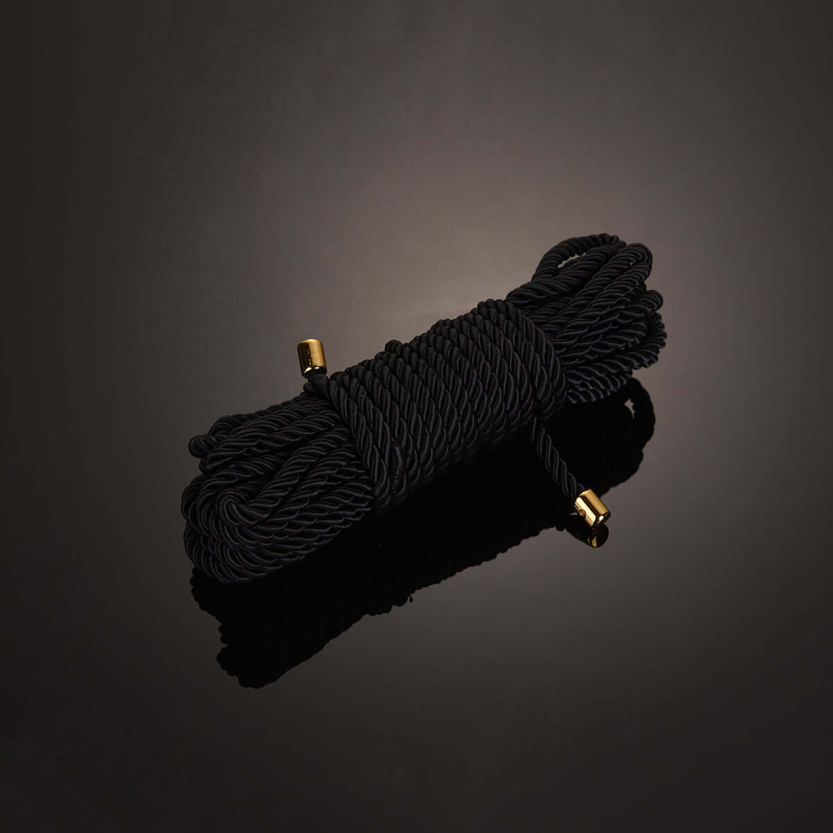 Luxurious black shibari bondage rope tied neatly with gold accents, ideal for workshops and educational purposes.
