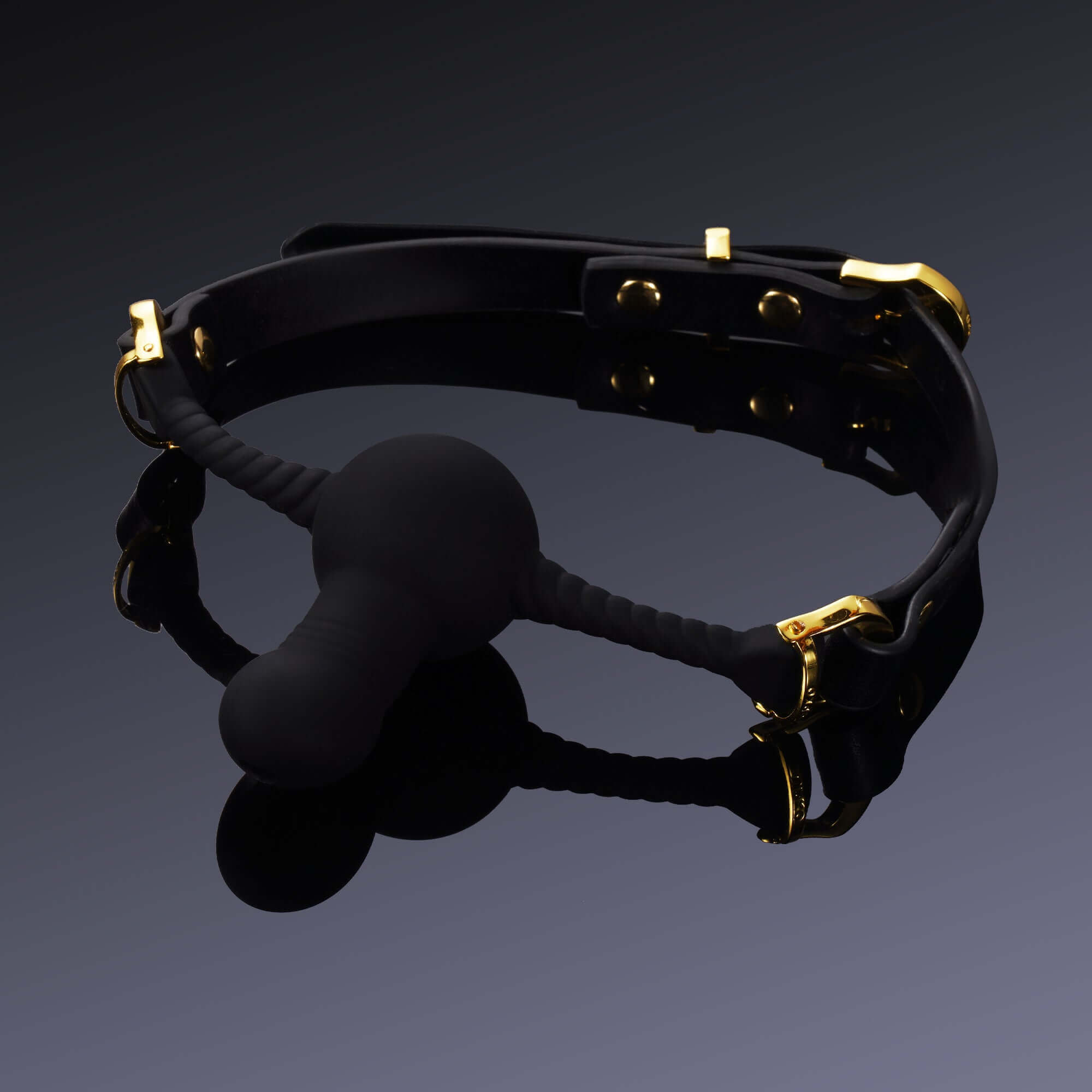 Black silicone dildo-shaped mouth gag with gold hardware accents on a black background.