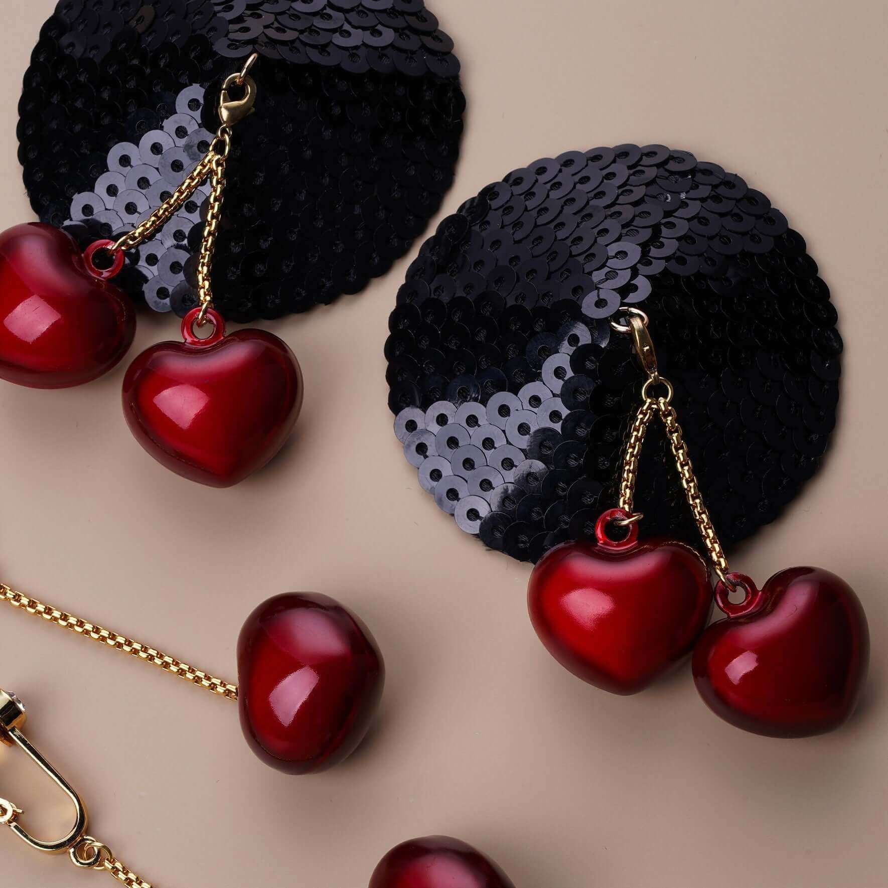 Black sequin nipple pasties with red heart charms and gold chains, showcasing stylish design and easy application.