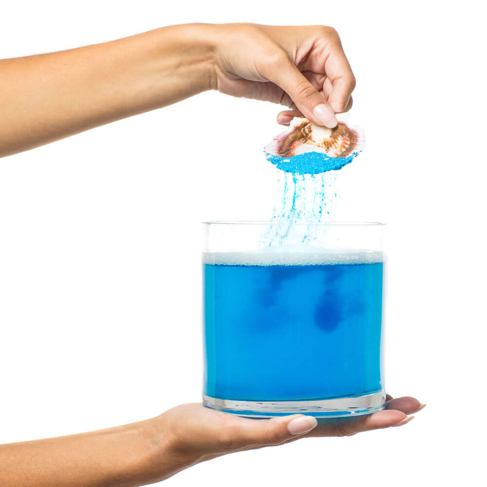 Kama Sutra Treasures of the Sea Bath Salts 24.5 Oz being poured into a blue bath water.