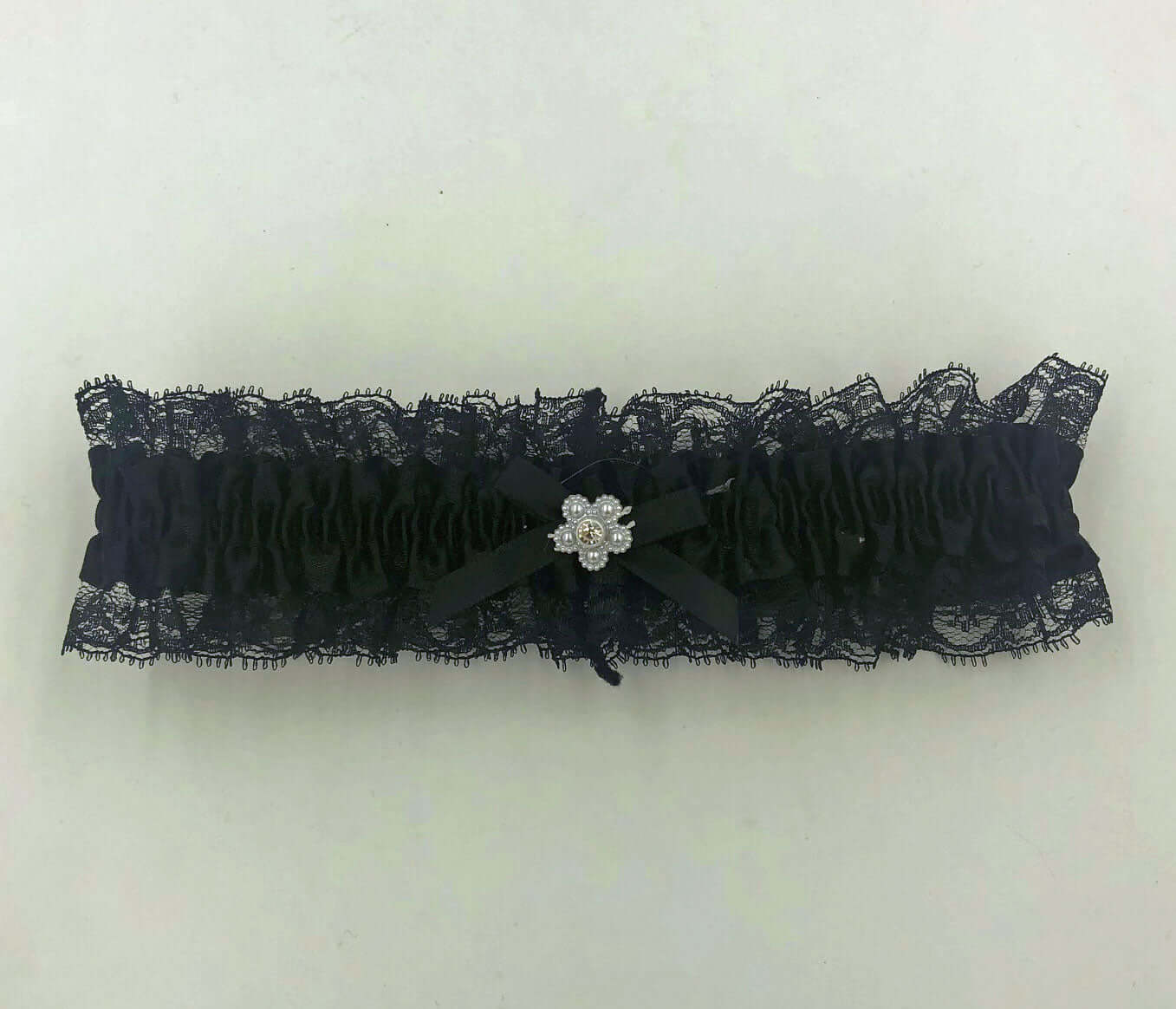 Black satin leg garter with black lace and floral embellishment, one size, 100% polyester, packaged in a display bag.