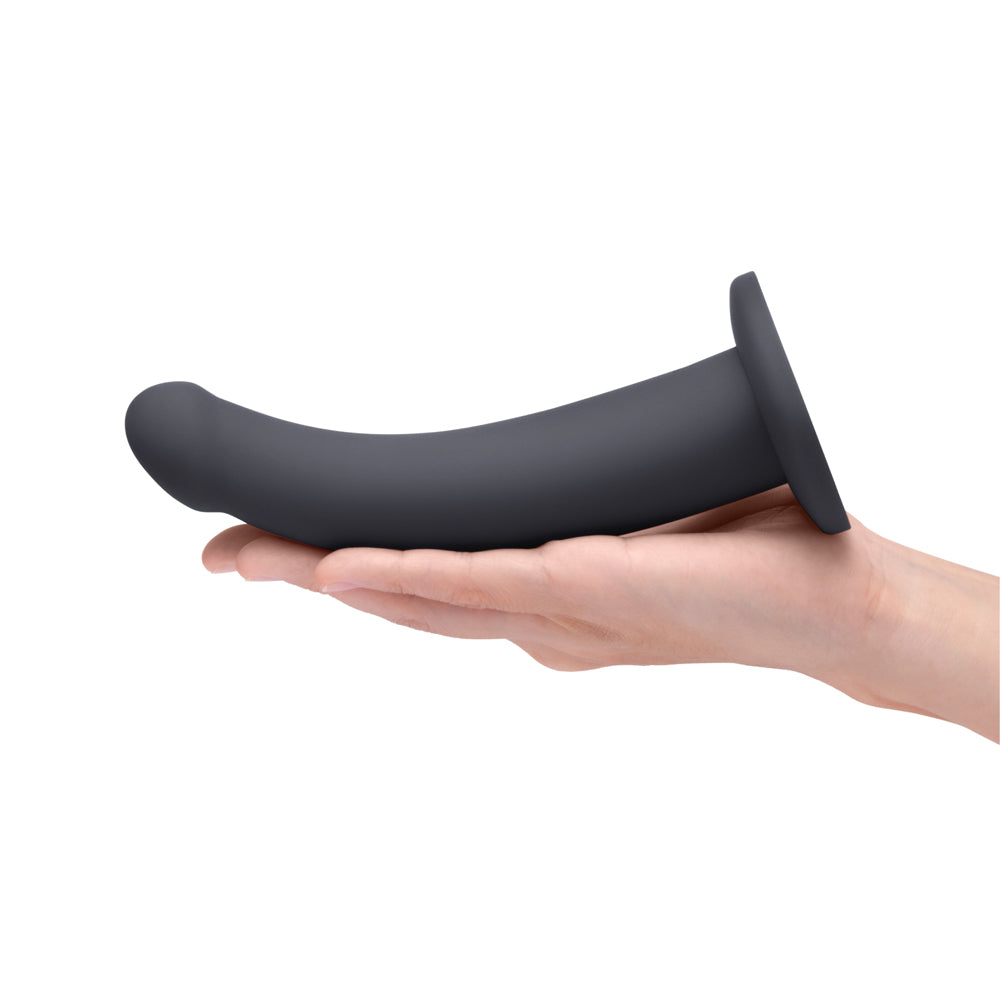 B-Vibe Essentials 7 Inch Smooth Silicone Dildo Black held in a hand, showcasing its sleek design and smooth surface.