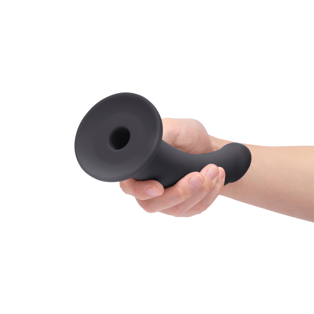 B-Vibe Essentials 7 Inch Smooth Silicone Dildo Black held in a hand, showcasing its sleek design and smooth surface.