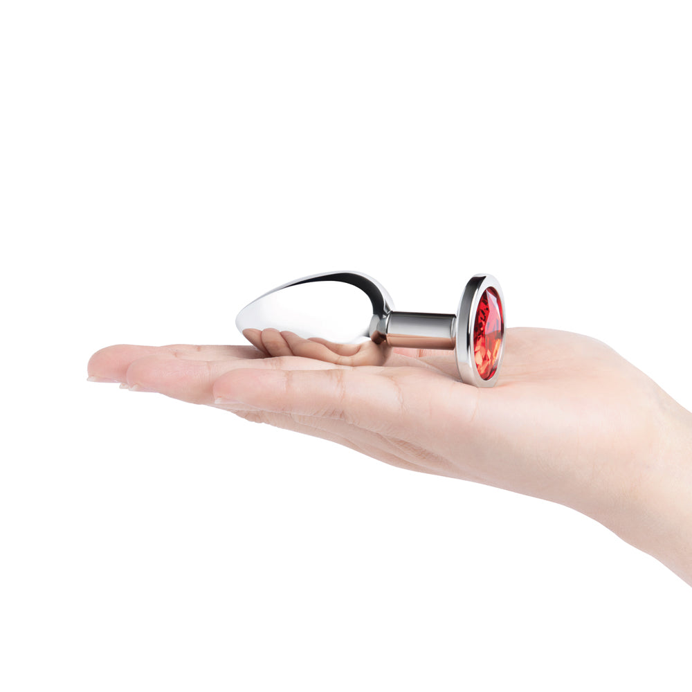 B-vibe 3.25 Inch Stainless Steel Jewel Butt Plug Red displayed in hand, showcasing its elegant design and red jewel base.