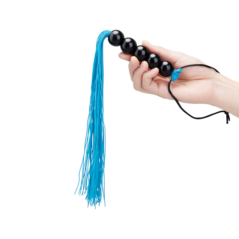 B-vibe Essentials Beaded Flogger in hand showcasing blue fringes and black beads for sensory play.