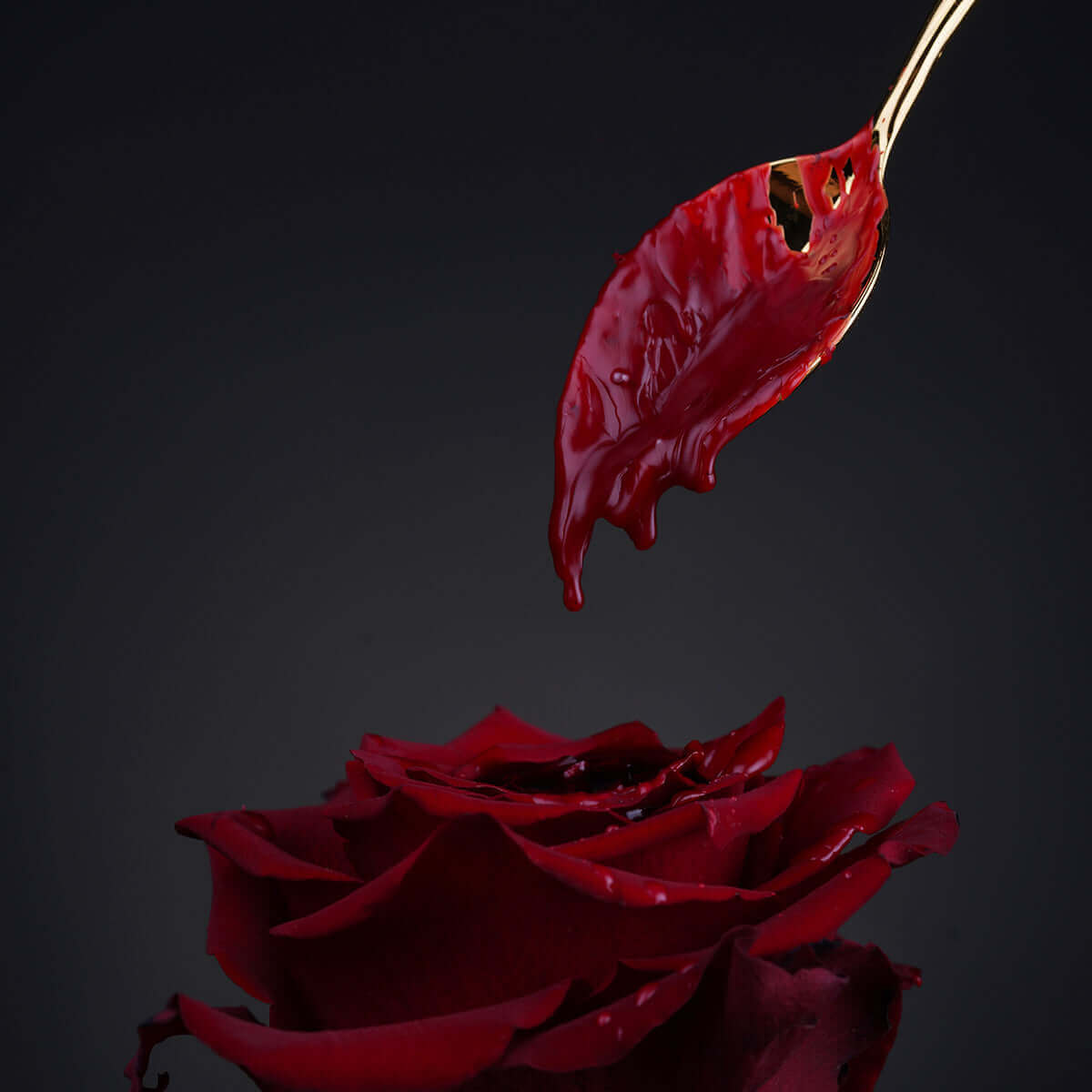 Close-up of a red rose with a spoon dripping red wax, creating an artistic and romantic atmosphere.