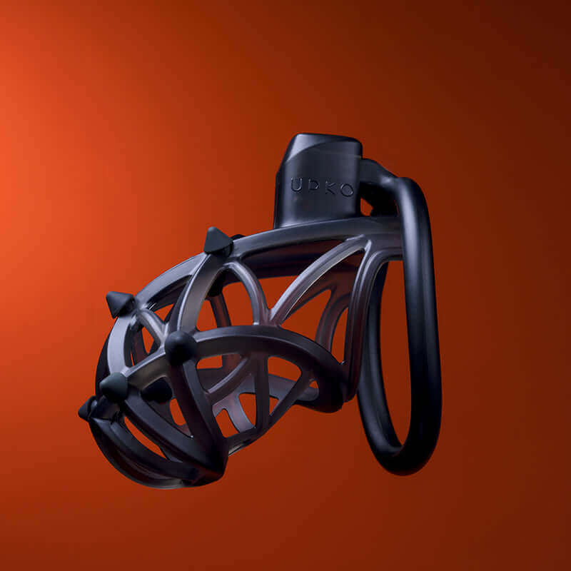 UPKO Caged Beast Male Chastity Device Kit in black against an orange background showcasing its unique design and structure.
