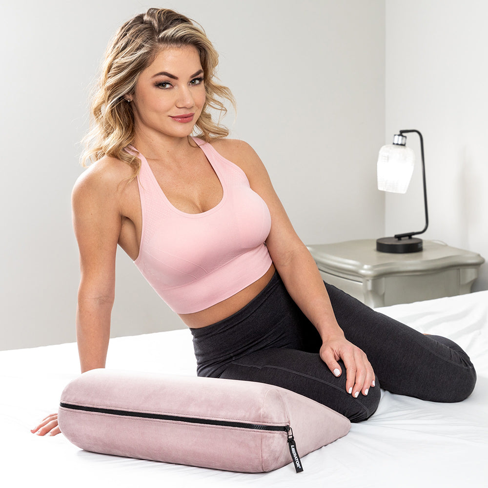 Liberator Jaz Original Rose Sex Positioning Pillow shown with a model in a bedroom setting.