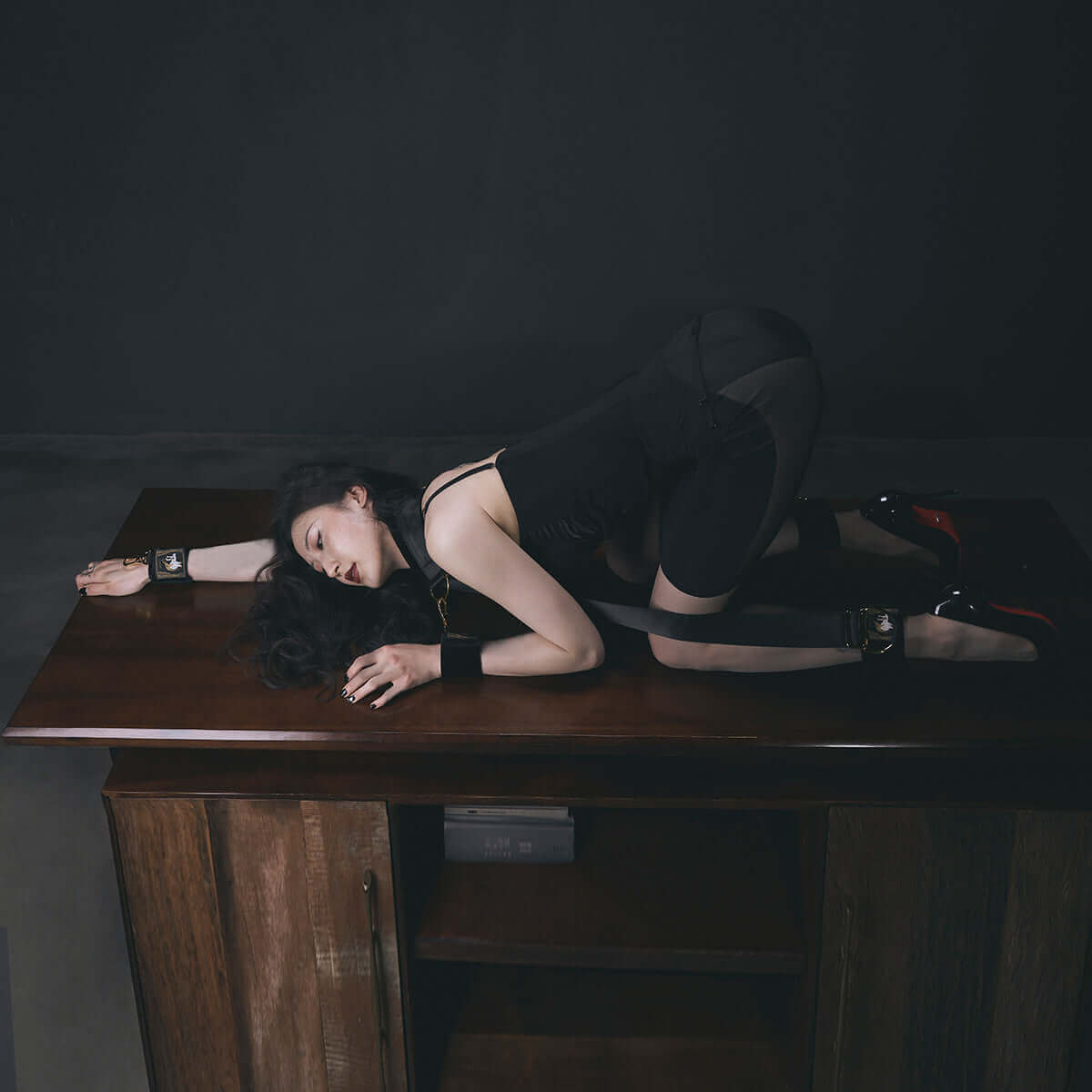 Woman in bondage cuffs positioned on a wooden table, showcasing UPKO Bondage Gear Sling with sleek design and function.