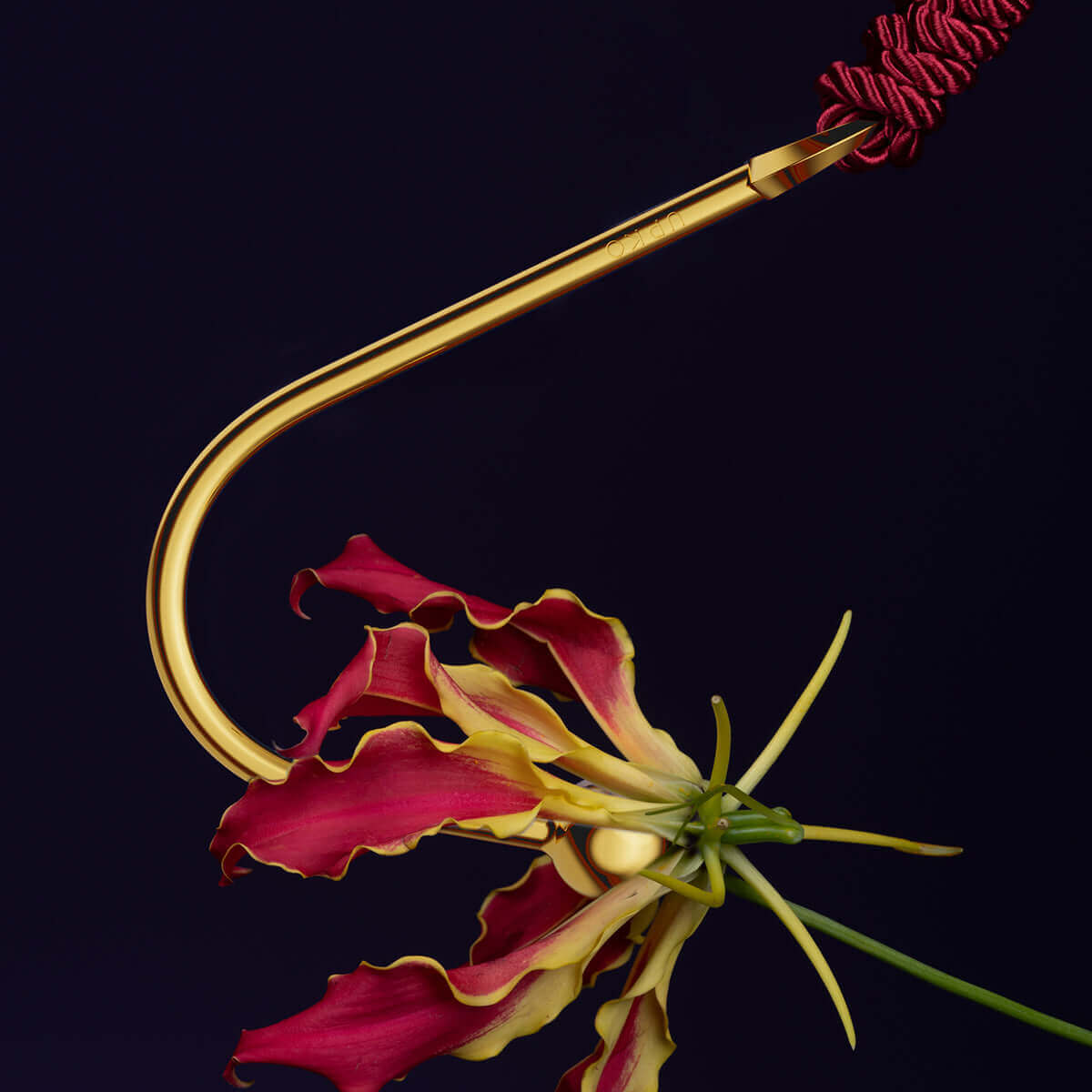 UPKO vaginal/anal hook in gold next to a vibrant flower, showcasing its sleek design for intimate use.
