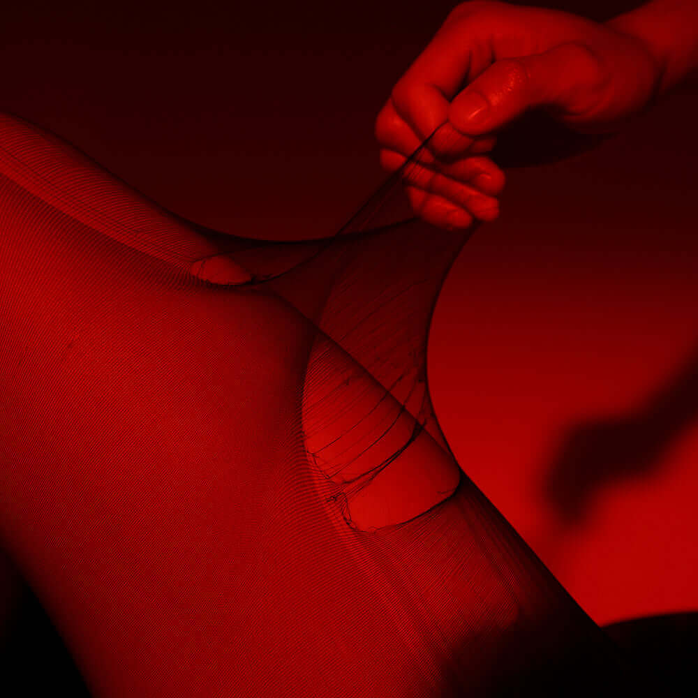 Hand pulling tear-away UPKO 5D tights against a red background, showcasing their unique design and comfort.