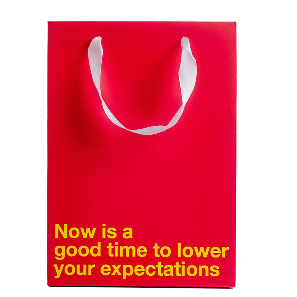 Lower Your Expectations Color Gift Bag Red featuring a humorous slogan for gifts and celebrations.