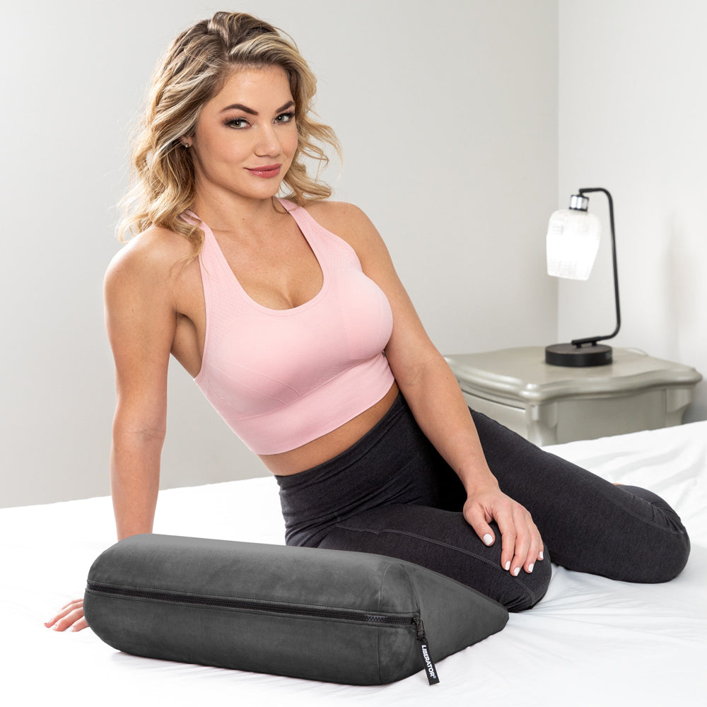 Liberator Jaz Original Sex Positioning Pillow Black on a bed with a woman in a pink top, showcasing its elegant design.
