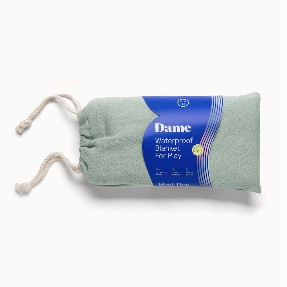 Dame Thro Waterproof Sex Blanket Sage rolled up, featuring a soft cotton exterior and waterproof protection for intimate moments.