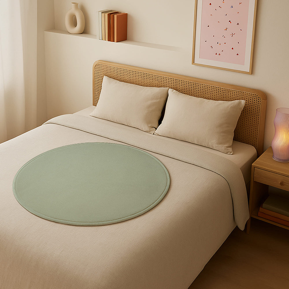 Dame Thro Waterproof Sex Blanket Sage on a bed, featuring a soft, circular design for comfortable intimate moments.