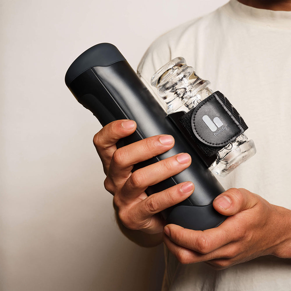 A person holding The Handy Interactive Stroker Black device with a transparent stroker attachment.