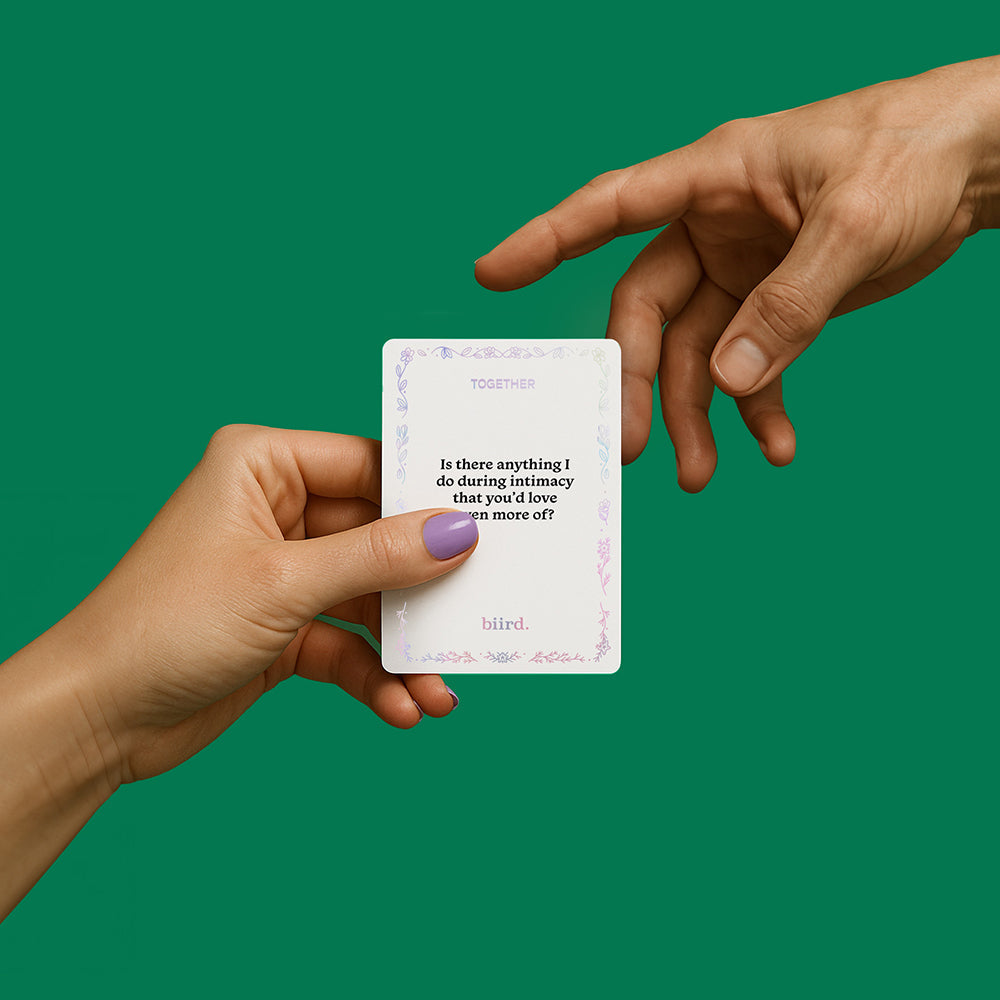 Biird X Jouissance Club Together Couples Card Game with hands holding a card on a green background.