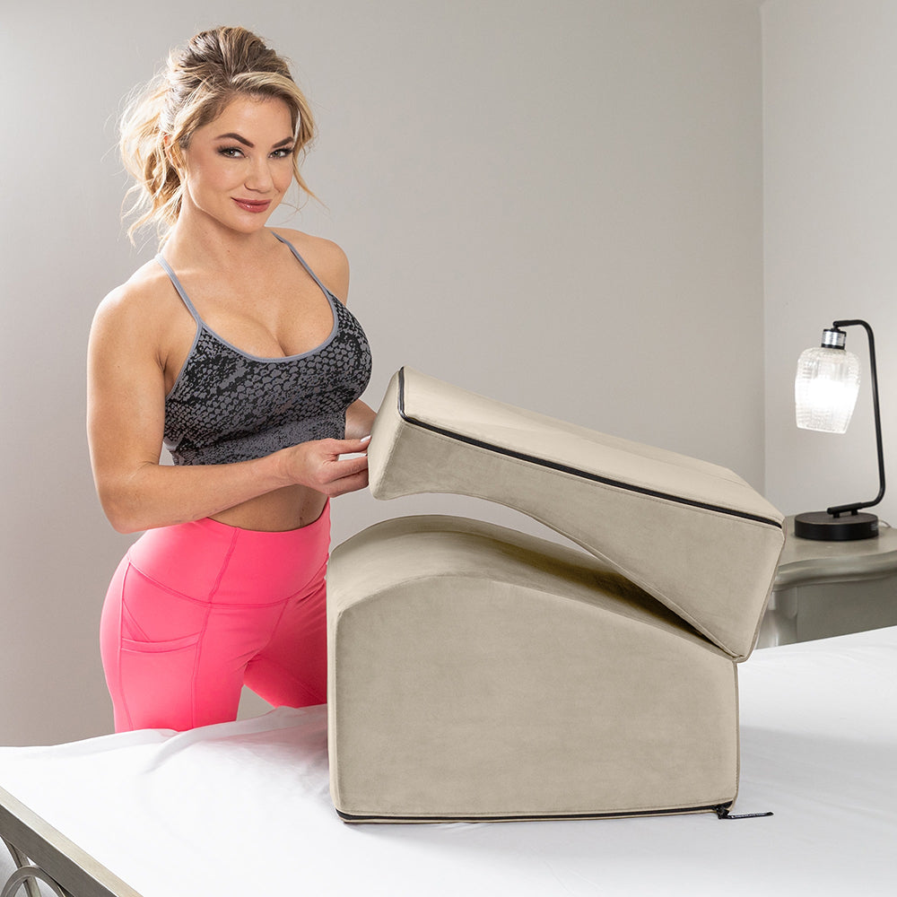 Liberator Flip Ramp Sex Positioning Pillow With Slip Cover Lush Cream displayed on a bed by a woman in workout attire.