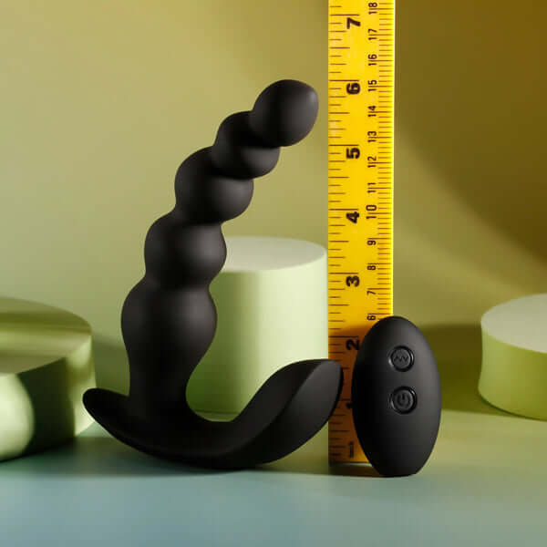 Black rechargeable silicone vibrating anal beads with remote control next to a ruler for size comparison.