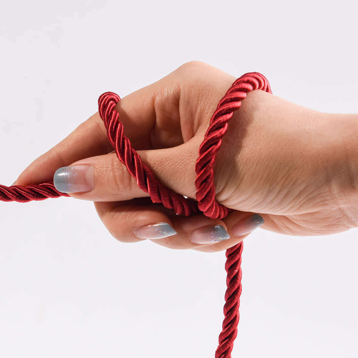 Hand holding luxurious red shibari bondage rope for workshops, showcasing softness and flexibility.