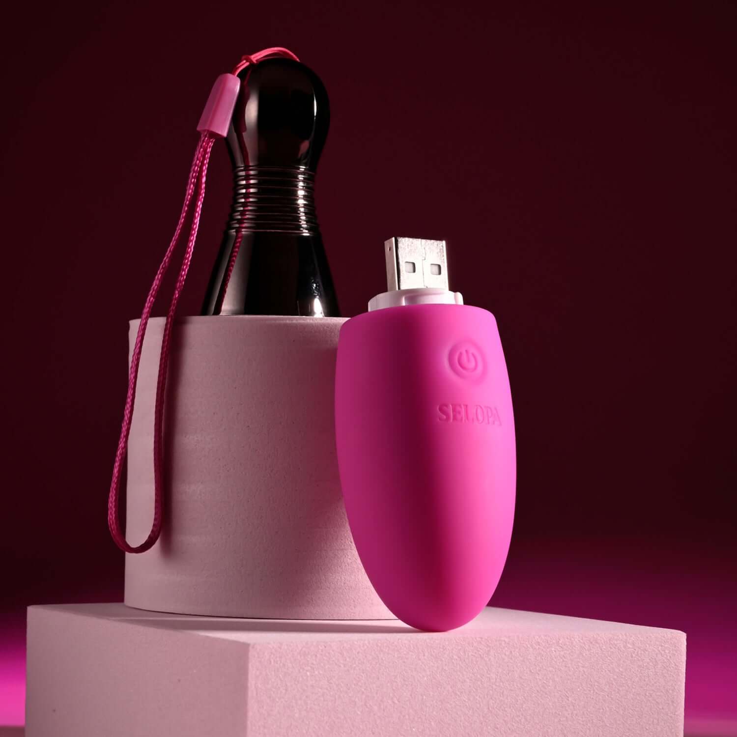 Pink companion bullet vibrator with USB connector and chrome handle on a pink display platform.