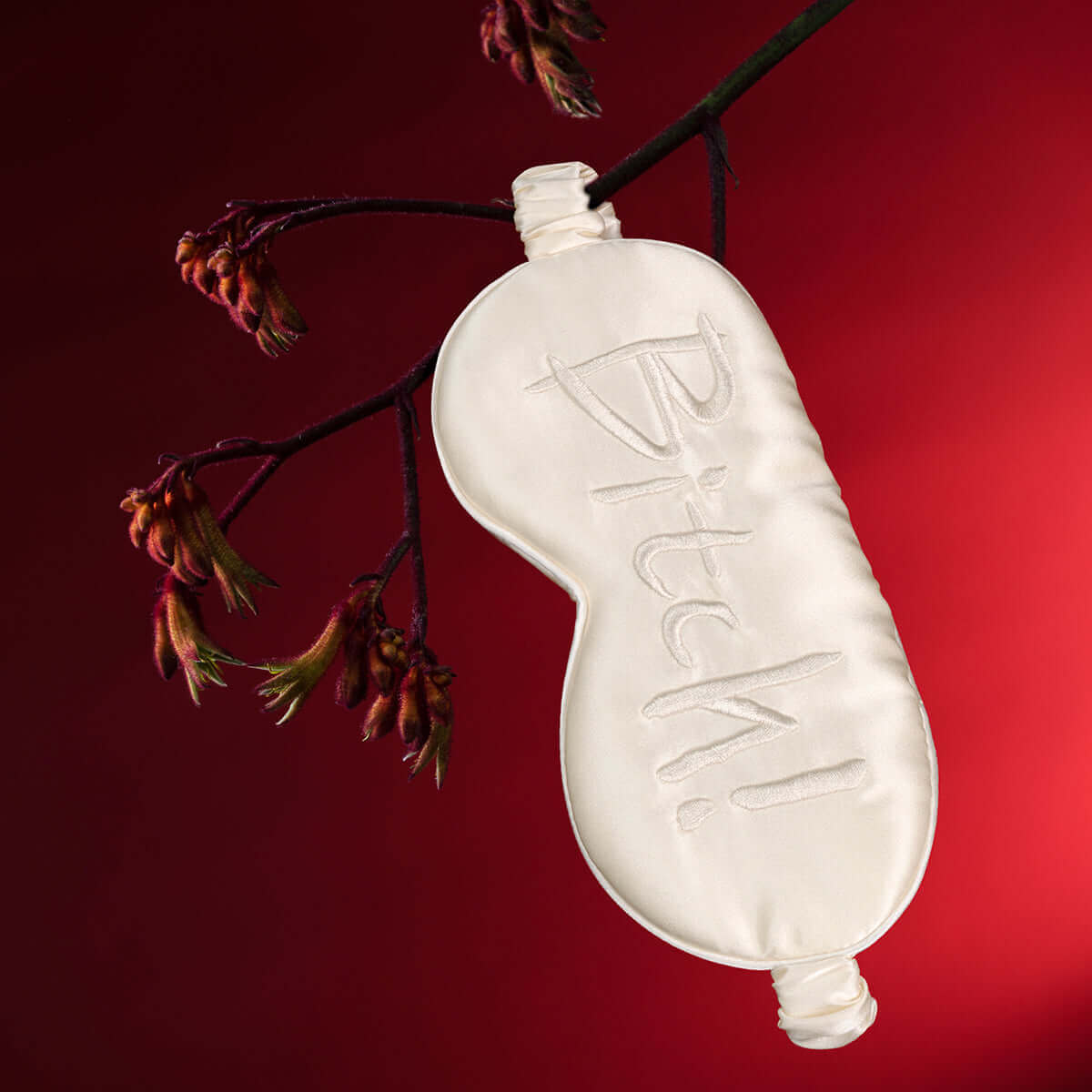 UPKO embroidered silk blindfold with "Bitch!" text, displayed on a branch against a dark red background. Super soft mulberry silk.