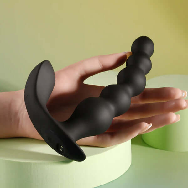 Black silicone vibrating anal beads with remote control, held in a hand on a colorful background.