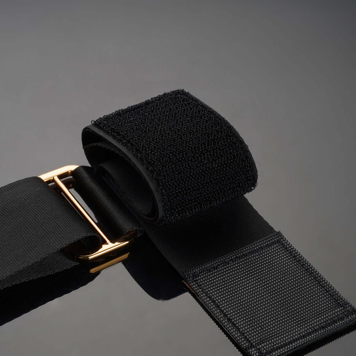 Close-up of UPKO black ankle restraint strap with gold buckle and textured fabric, ideal for S&M play.