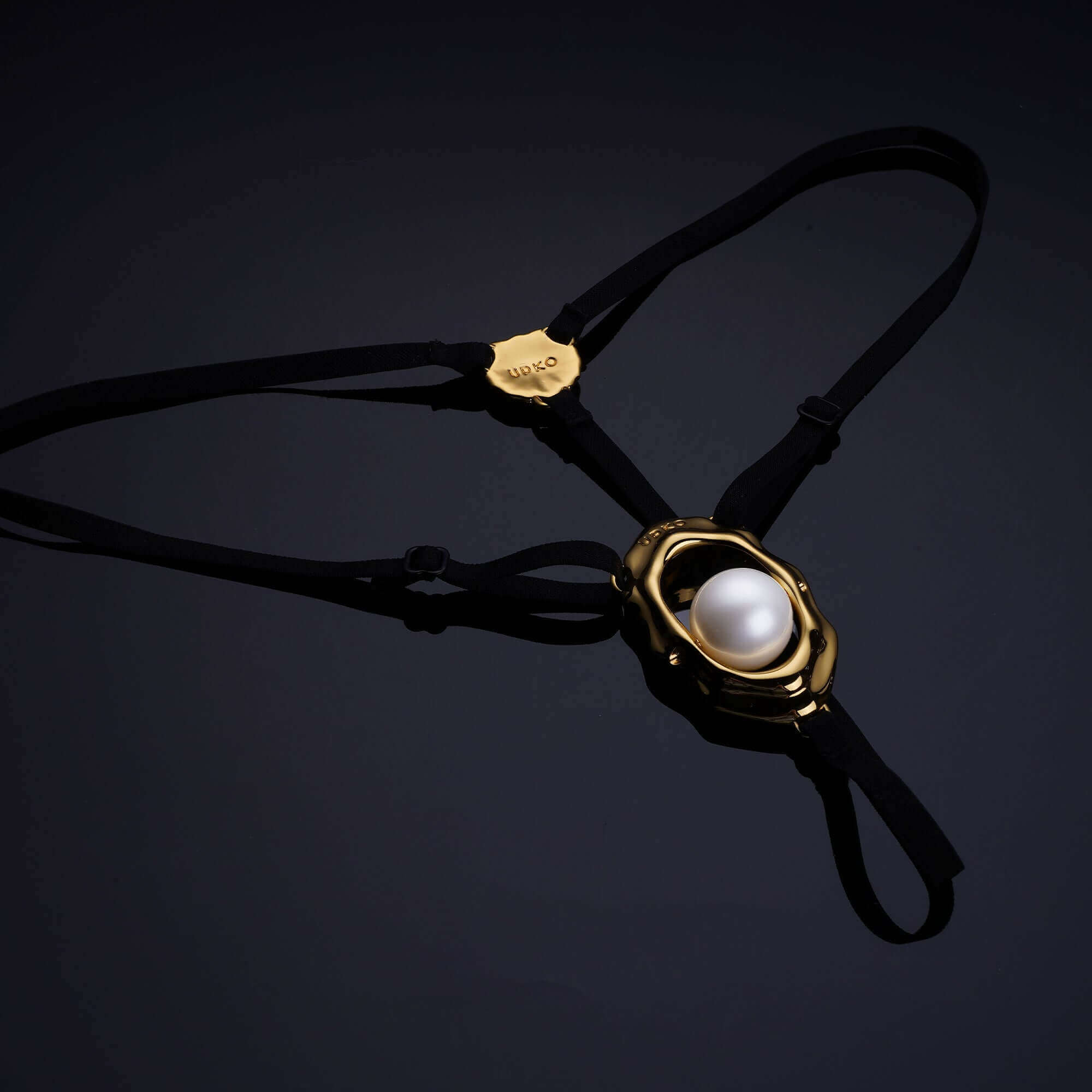 Moist Eyes G-string clitoral jewelry with bead stimulator and gold seashell embellishments on a black background.