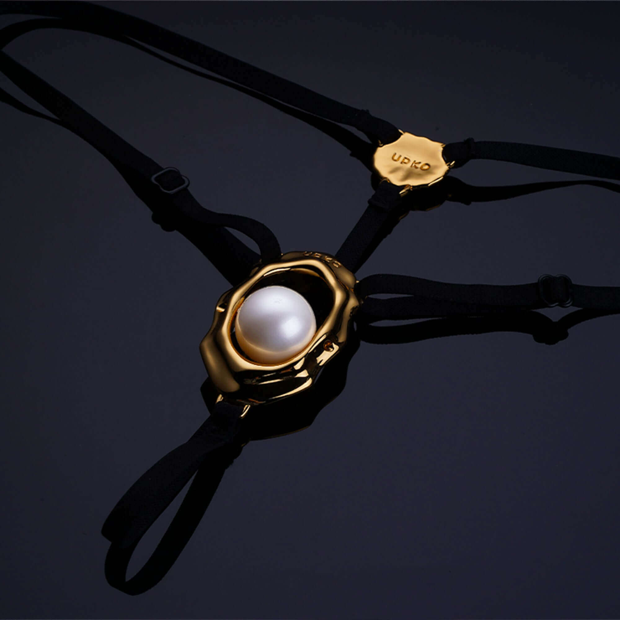 "Moist Eyes" G-string clitoral jewelry featuring a gold seashell design and pearl bead stimulator on black straps.