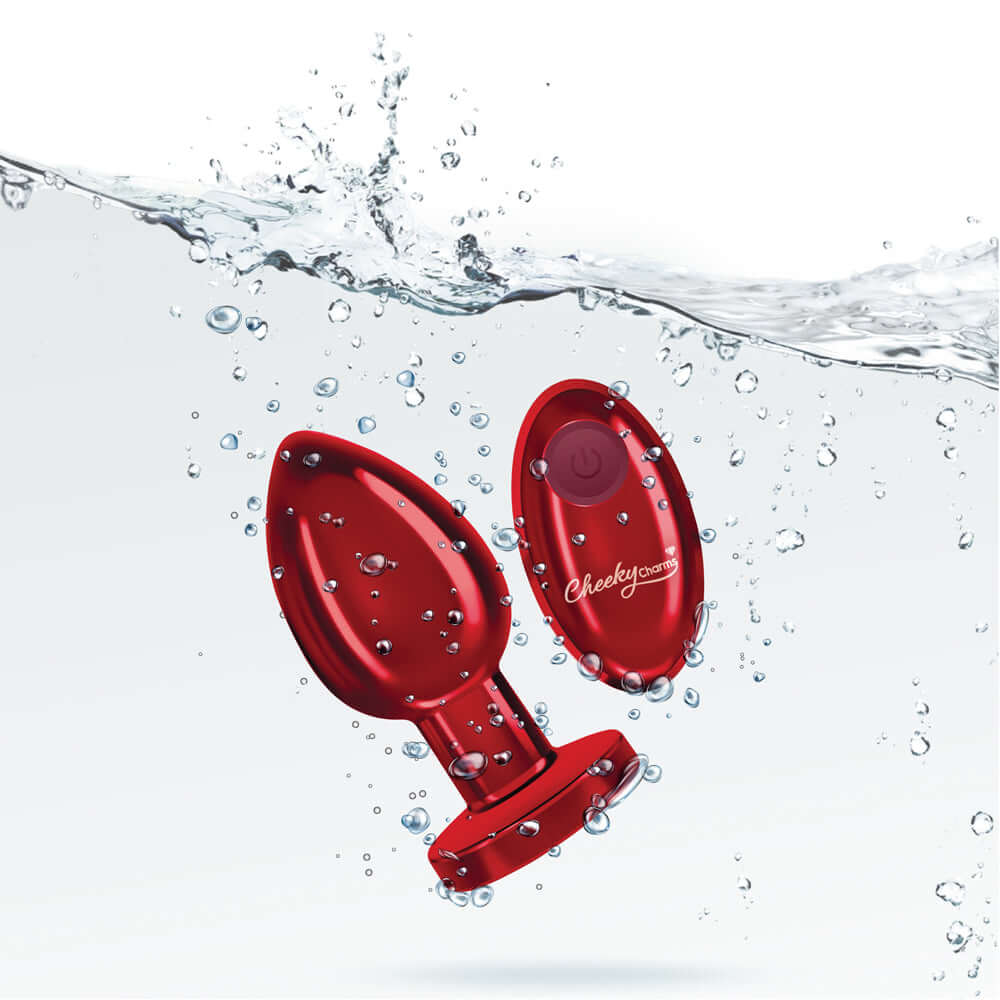 Cheeky Charms large rechargeable vibrating metal butt plug with remote control in red, submerged in water with bubbles.