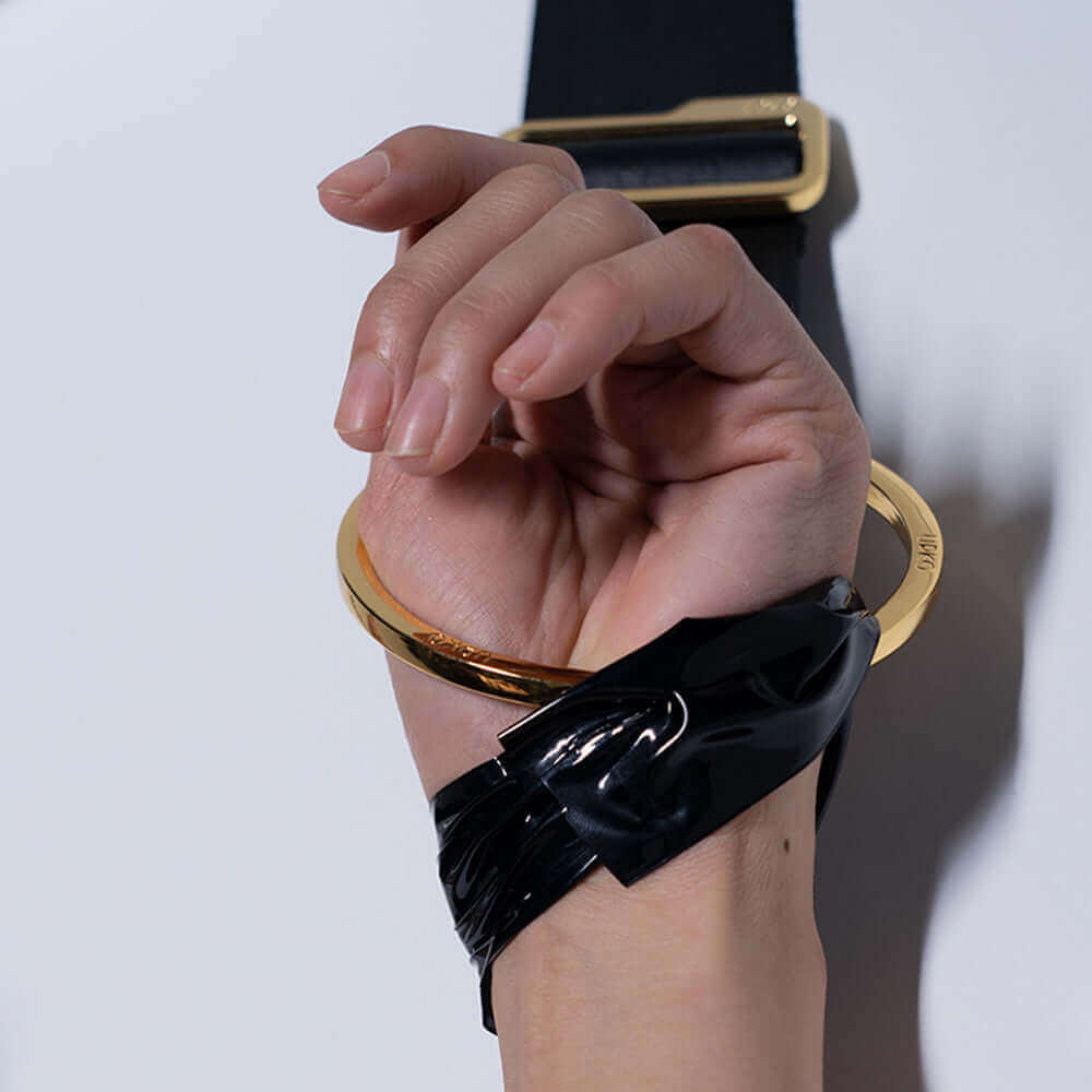 Hand with gold cuff and black tape, showcasing UPKO Over the Door Pair Wrist Restraints for bondage play.