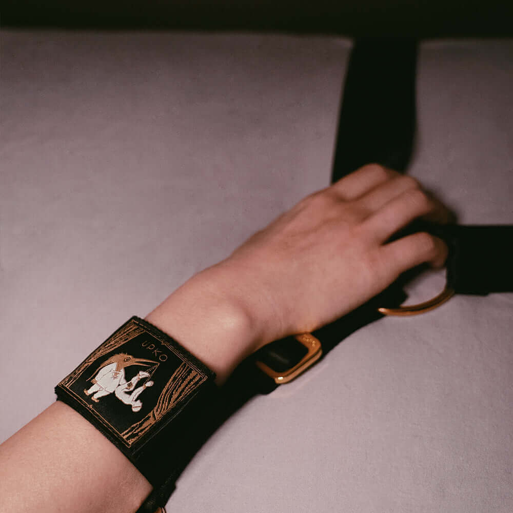 Hand wearing UPKO adjustable bed restraint strap, showcasing black and gold design for BDSM comfort and style.