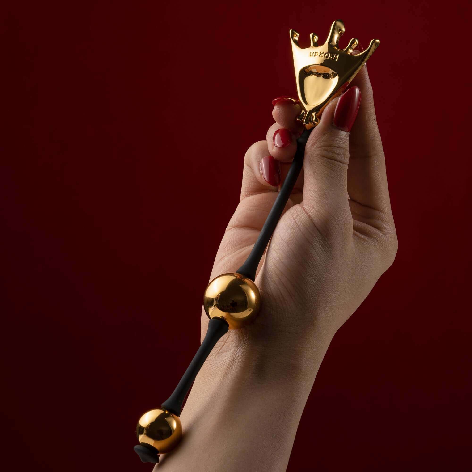 Hand holding the Queen Premium Metal Pleasure Balls from the "Chess" Collection on a red background.