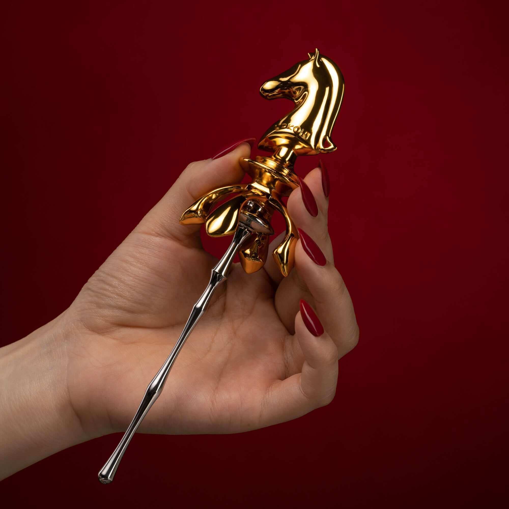 Golden knight urethral sound in a hand against a red background, part of "The Chess" collection.