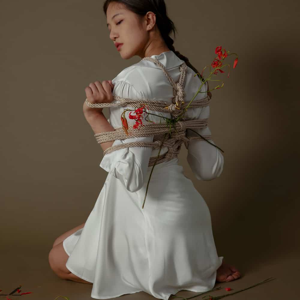 Woman in a white dress artfully tied with Shibari rope, showcasing elegance and creativity in bondage practice.