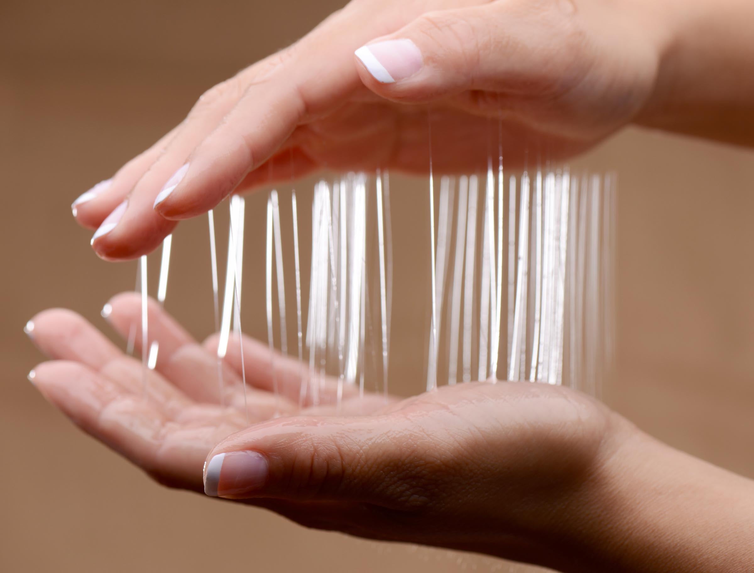 Hands holding thin, clear massage gel strands for Nuru Inflatable Massage Sheet Deluxe Kit.