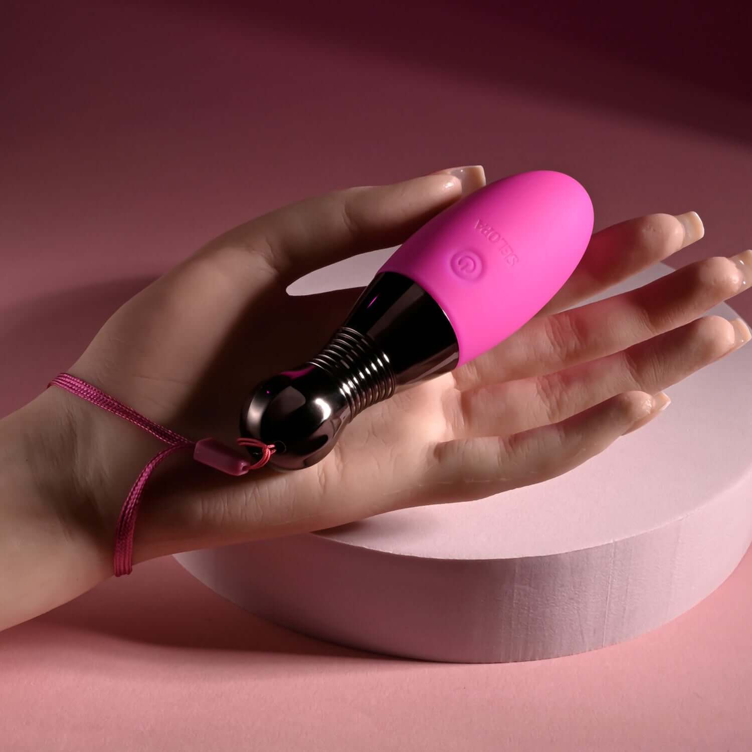 Pink companion bullet vibrator held in a hand, showcasing its sleek design and chrome finish against a pastel background.