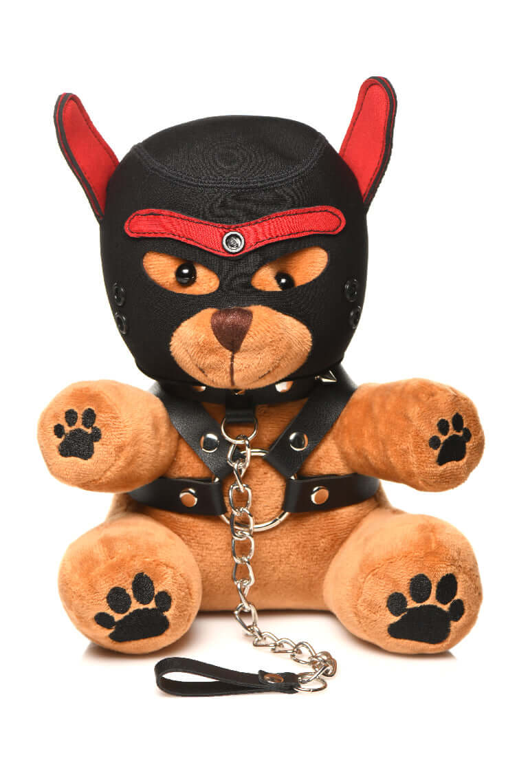 Stuffed bear with light peach fur wearing a black puppy mask, faux leather harness with metal O-rings, and chain leash.