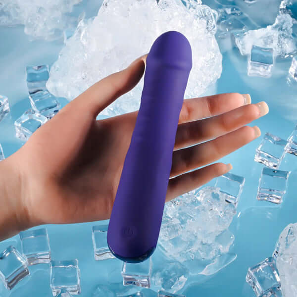 Hand holding a purple rechargeable silicone thrusting vibrator against a backdrop of ice cubes.