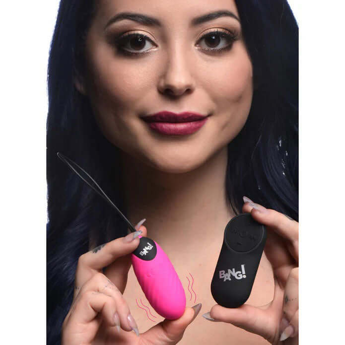 Woman holding the Bang 28x Swirl Silicone Egg Vibrator Pink and its remote control.