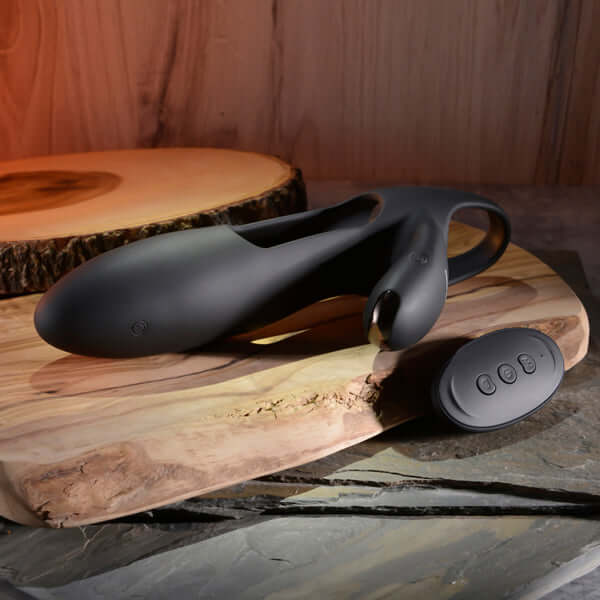 Zero Tolerance Nautilus Rechargeable Silicone Dual Cock Ring in black on a wooden table with remote control.