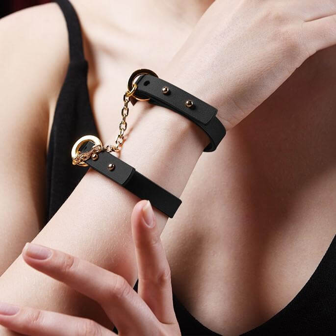 UPKO luxury Italian leather black handcuff bracelets with gold chain, worn elegantly on a woman's wrist.