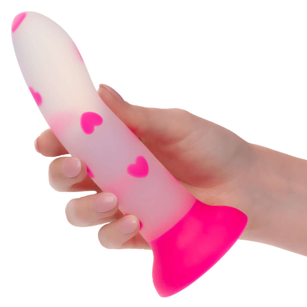 Pink glow stick heart dildo with glow-in-the-dark heart pattern, made of ultra-soft satin finish silicone, held in a hand.